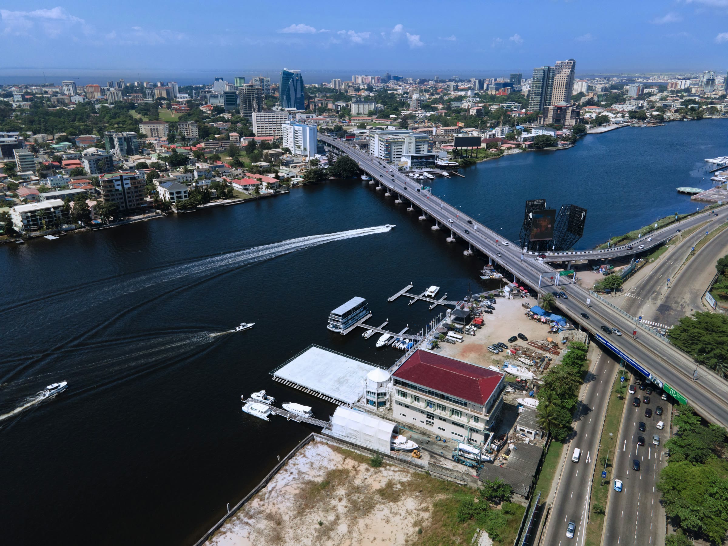 Aerial view of Victoria Island, Lagos, with boats crossing the lagoon and the city skyline beyond.